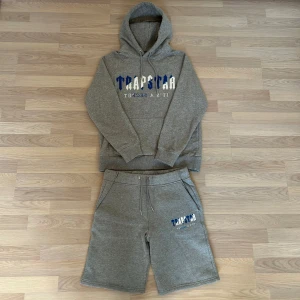 Grå Tracksuit Trapstar med blå/vit text - Säljer en grå tracksuit från Trapstar med broderad text i blått och vitt på bröstet. Perfekt för sommarn. Helt ny och oanvänd. Fraktar inom 24 timmar efter köp🌟