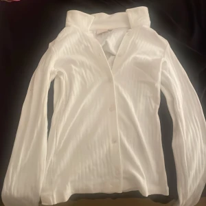 Vit ribbad skjorta från Nelly XS - Säljer en vit långärmad skjorta från Nelly i storlek XS. Skjortan har ribbat tyg med diskreta vertikala ränder och klassisk krage. Stängs med knappar framtill och är perfekt för en clean och stilren look.
