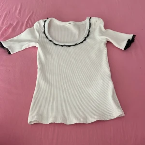 Vit ribbad topp med spetsdetaljer - Supersöt vit ribbad topp med svarta spetsdetaljer vid halsringning och ärmslut.