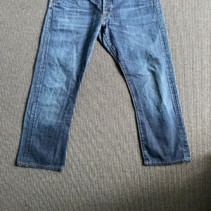 Blå jeans från Replay Denim - Säljer ett par klassiska blå jeans från Replay Denim med raka ben och snygga detaljer på bakfickorna. Jeansen har normal passform och är tillverkade i slitstarkt denimtyg. Perfekta för dig som gillar en tidlös och avslappnad stil.