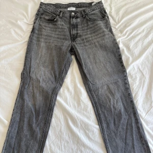 Grå jeans från Vaillent, rak modell - Säljer ett par grå jeans från Vaillent i rak modell. Jeansen har klassisk femficksdesign, bälteshällor och dragkedja med knapp. Materialet är denim i bomull och färgen är tvättad grå med svarta sömmar. Perfekta för en avslappnad och stilren look.