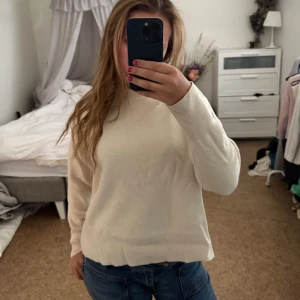 Beige stickad tröja - En stilren beige stickad tröja med högre ribbad krage och långa ärmar. Tröjan har en relaxed passform och bred ribbad kant nedtill och vid ärmsluten. Perfekt att matcha med jeans för en enkel och snygg look. Svårt märkbara fläckar som möjligtvis går bort i en bra tvätt, men annars är de inte så tydliga, använt fåtal gånger. Klippt bort storlekslappen men brukar ha S i liknande tröjor för referens