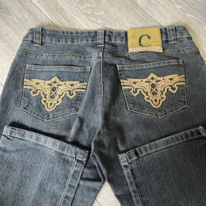 Grå jeans från Central Jeans med brodyr - Snygga grå jeans från Central Jeans med guldigt broderi på bakfickorna och en unik gul patch med C på linningen. Klassisk femficksmodell i jeansmaterial och raka ben. Perfekta för dig som vill sticka ut lite extra med detaljer.