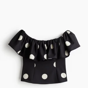 prickig topp - Snygg svart offshoulder topp med vita prickar och volang runt axlarna. Perfekt för dig som vill sticka ut med en lekfull och trendig stil. Toppen har en figurnära passform.