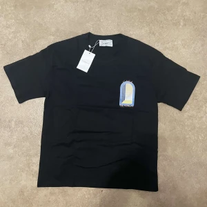 Svart t-shirt från Casablanca - Svart t-shirt från Casablanca med färgglatt tryck av en öppen dörr i blått, gult och vitt på både bröstet och ryggen. Klassisk passform med rund hals och korta ärmar. Perfekt för dig som gillar stilrena plagg med unik twist.