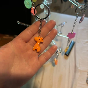 Nyckelring med orange giraff - Söt nyckelring med en liten orange giraff i plast. Giraffen har rosa prickar och svarta ögon, och hänger i en silverfärgad kedja. Perfekt att fästa på väskan eller nyckelknippan för en lekfull touch.