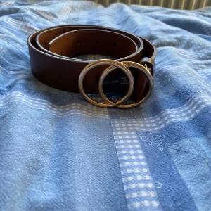 Brunt skärp med dubbla ringar - Snyggt brunt bälte i skinn med två runda metallringar som spänne. Bältet har en stilren och enkel design som passar till många olika outfits. Perfekt accessoar för att lyfta din look med en trendig detalj. Jag har gjort extra hål 