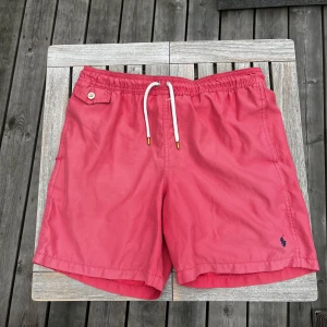 Polo Ralph Lauren badshorts - Rosa badshorts från Polo Ralph Lauren med vit snörning i midjan och klassisk logga broderad i mörkblått. Bra skick. Fråga vid funderingar. 