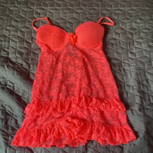Röd spetsklänning med volanger - Söt röd kortklänning i spets med volangdetaljer och tunna axelband. Klänningen har vadderade kupor, liten rosett framtill och öppen rygg med knäppning. Perfekt för dig som gillar romantisk och feminin stil.