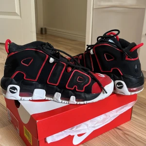 Nike Air More Uptempo svart/röd - Nike Air More Uptempo sneakers i svart med röda och vita detaljer. Tjock sula med synlig Air-enhet, stora AIR-bokstäver på sidorna och klassisk swoosh-logga. Skorna har snörning och en sportig vibe, perfekta för dig som gillar statement sneakers.