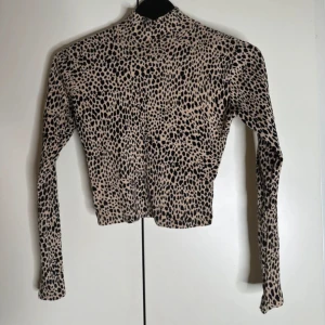 Leopardmönstrad polotopp i beige och svart - Snygg polotopp med leopardmönster i beige och svart. Toppen har lång ärm och croppad passform, helt perfekt men tyvärr för liten för mig. 
