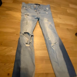 ljusblå jeans - Ljusblåa lågmidjade Hollister Vintage Boyfriend jeans med slitningar och hål på benen för en cool, avslappnad look. Byxorna har klassisk femficksdesign, bena på byxorna är utsydda till bootcut Jeans. 