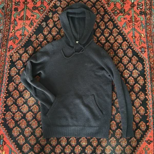 Svart hoodie från MC2 Saint Barth - Mysig svart hoodie från MC2 Saint Barth i stickad ull. Tröjan har huva med snörning, broderad logga på bröstet och en klassisk känguruficka framtill. Perfekt för kyliga dagar och enkel att matcha med jeans eller joggers.