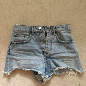  jeansshorts från Zara - Snygga ljusblå jeansshorts från Zara med fransiga kanter. Klassisk femficksmodell med knappar framtill och bälteshällor. Perfekta för sommaren och ger en avslappnad vibe.