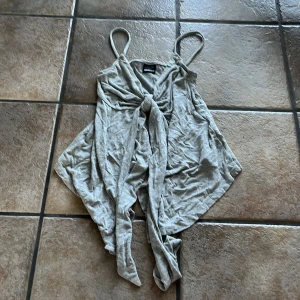 Grå knytlinne från Gina Tricot - Supersöt ljusgrå linnetopp från Gina Tricot med smala axelband och snygg knytning framtill. Toppen har en flowy passform med spetsig nederkant. Perfekt för varma dagar och enkel att styla med jeans eller kjol.