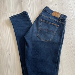Nudie jeans tight terry - Snygga mörkblå jeans från Nudie med klassisk femficksdesign och kontrastsömmar. Jeansen har en smal passform, normal midja och är tillverkade i stretchig denim för extra komfort. Perfekta för dig som gillar en stilren och modern look. Modellen tight terry, skinny fit. Nästan helt oanvända och ser nya ut, 10/10 skick! Storlek 33/34.