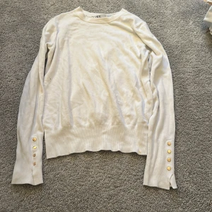 Vit tröja från Zara med guldknappar - Vit långärmad tröja från Zara med rund halsringning och snygga guldknappar på ärmsluten. Tröjan har en klassisk passform och är tillverkad i mjukt material som känns skönt mot huden. Perfekt för dig som gillar stilrena detaljer.