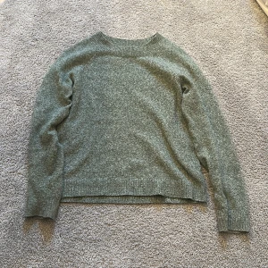 Grön stickad tröja med rund hals - Mysig grön stickad tröja med rund halsringning och långa ärmar. Tröjan har en enkel och stilren design med ribbade muddar vid ärmslut och nederkant. Perfekt för lager-på-lager under kyliga dagar.