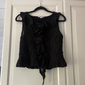 Svart volang topp från Gina Tricot - Superfin svart ”kort” topp från Gina Tricot i storlek 158/164. Den är lätt strukturerad och har små volangdetaljer längst ned. Använd fåtal gånger. Skriv om du har några frågor💕💕