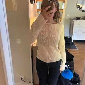 Krämvit ribbad långärmad topp - Säljer en krämvit långärmad topp med coolt vågigt ribbat mönster. Toppen har en något bredare rund halsringning och sitter snyggt med en slim passform. Perfekt att styla med jeans eller kjol för en clean look.