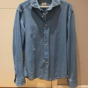 Blå skjorta från La Chemise - Snygg blå skjorta i denim-style från La Chemise (modell Norrmalm) i slim fit-modell. Skjortan har klassisk krage, långa ärmar och knäppning framtill. 