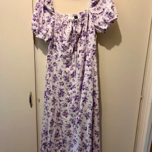 Ny klänning strl XL - Helt ny lila blommig klänning i strl XL. Material: polyester och elastan  - Slits ena sidan framtill - Dragkedja i ryggen   Jag är 160 cm lång för referens. 