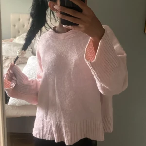 Ljusrosa stickad tröja med vida ärmar - Supermysig ljusrosa stickad tröja med breda ribbade muddar vid ärmslut och nederkant. Tröjan har en loose passform och är långärmad, perfekt för att chilla eller hänga med vänner. Enkel och stilren design som är lätt att matcha.