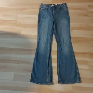 Blå flare jeans från H&M, high waist - Snygga blå jeans från H&M med flare-ben och hög midja. Jeansen har justerbar midja och klassisk femficksdesign. Perfekta för dig som gillar en retro vibe och vill ha ett par bekväma och trendiga jeans i garderoben.
