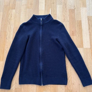 Mörkblå stickad kofta från deFacto - mörkblå stickad zip tröja från deFacto med hel dragkedja framtill och ribbad krage. Koftan har långärmad design och ett strukturerat mönster i tyget. Passar runt 170-174 cm, skick: 8/10, Vill man ha fler bilder så tveka inte att skriva! Perfekt för dig som gillar en stilren och fräsch look🌟🌟