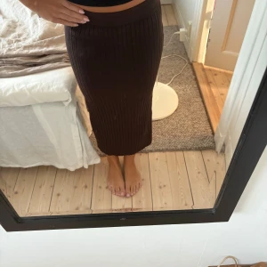 Brun långkjol - Säljer en mörkbrun, ribbstickad långkjol från Lindex. Kjolen har en hög midja och är figurnära med stretchigt material som är perfekt till höst och sommar. 