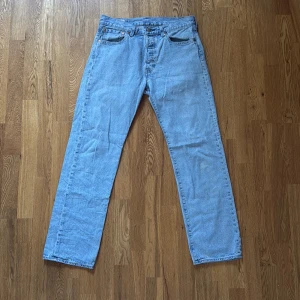 Levi's 501 ljusblå jeans W32 L32 - Klassiska Levi's 501 jeans i ljusblå denim. Köpa för 1100kr. Rak passform med fem fickor, knappgylf och ikonisk läderpatch bak i midjan. Perfekta för en avslappnad och tidlös stil. Finns två mindre synliga fläckar på västra underbenet, se bild nummer 5. Annars bra skick! Skriv gärna om ni har en fråga☺️