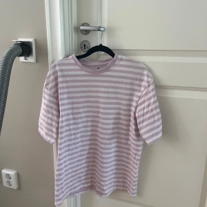 Randig ljusrosa t-shirt från H&M - Säljer en chill t-shirt från H&M med ljusrosa och vita horisontella ränder. Klassisk rund hals och korta ärmar, perfekt för en avslappnad stil. Mjuk bomull som känns skön mot huden. Passar dig som gillar enkel och fräsch look.