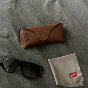 Svarta Ray-Ban Wayfarer solglasögon - Säljer ett par klassiska svarta Ray-Ban Wayfarer solglasögon med breda bågar och mörka linser. Kommer med original brunt fodral i skinn och putsduk med Ray-Ban-logga. Perfekt för dig som vill ha en tidlös och cool look. 100 procent äkta pris 800 men kan diskuteras 