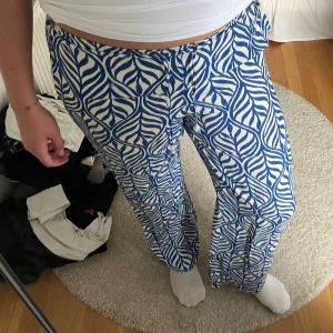 Blåvita mönstrade wide byxor - Säljer ett par blåvita byxor med ett coolt grafiskt mönster som påminner om blad eller zebra. Byxorna har en loose och wide passform med rak siluett och elastisk midja. Perfekta för dig som gillar att sticka ut med färg och mönster.
