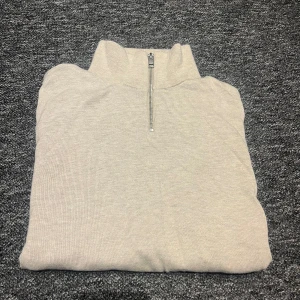 Beige half zip tröja Jack & Jones - Snygg beige stickad tröja från Jack & Jones med half zip-dragkedja och hög krage. Perfekt för lager-på-lager och chill stil. Tröjan är i mjukt material och har en clean look utan mönster eller extra detaljer.