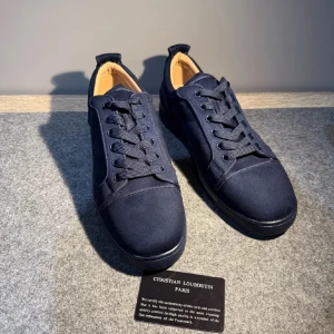 Mörkblå sneakers från Christian Louboutin - Säljer ett par stilrena mörkblå sneakers från Christian Louboutin med snyggt broderad logga på hälen. Skorna har rund tå, platt sula och är tillverkade i mjuk mocka med matchande snörning. Insidan är beige och ger en lyxig känsla. Perfekta för dig som gillar exklusiva detaljer.