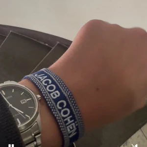 Blått armband från Jacob Cohën - Snyggt blått armband från Jacob Cohën med vit broderad logga. Armbandet är gjort i textil och har en justerbar knytning för perfekt passform. Perfekt accessoar för att lyfta din outfit med en cool detalj. Köpte ett par Jacob Cohën jeans och fick med armbandet då ifrån butiken Lucca vilket bevisar på att den är 110% äkta, går också inte att köpa separat man får bara ett sånt armband om man köper en viss modell av Jacob Cohën. (PRIS KAN DISKUTERAS)