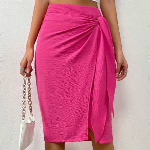 Rosa omlottkjol med knyt - Snygg rosa omlottkjol med knyt i sidan och slits framtill. Kjolen har en lätt skrynklig struktur och sitter tajt över höfterna. Perfekt för dig som vill sticka ut med en färgstark look. OANVÄND 