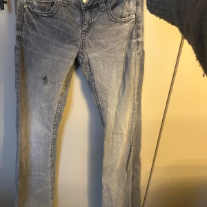 Grå jeans från Gina Tricot, stl 152 - Snygga grå jeans från Gina Tricot i storlek 152. Modellen har klassisk femficksdesign, tajta men utsvängda nertill och ett litet hål på ena låret som man lätt kan sy eller gör till ett större hål. Jeansen har silverfärgade knappar på fram och bakfickor. Perfekta till en avslappnad streetstil, Priset kan diskuteras.