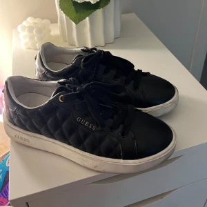 Svarta sneakers från Guess - Snygga svarta sneakers från Guess med quiltad sida och vita sulor. Skorna har snörning och diskret logga i guld på sidan. Använda ett ett fåtal gånger💗