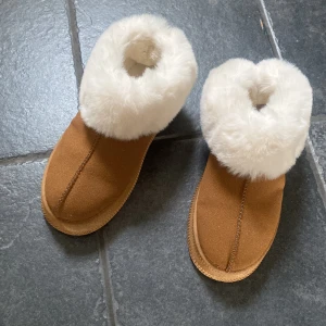 Bruna boots med vit fuskpäls - Mysiga bruna boots med fluffig vit fuskpäls runt öppningen. Skorna har en platt sula och är perfekta för kalla dagar. insidan är fodrad för extra värme. Snyggt och stilrent val för vintern.