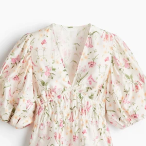 Blommig blus med puffärm från H&M - Supersöt blommig blus från H&M i ljusa färger med rosa och gula blommor. Blusen har v-ringning, puffiga trekvartsärmar och smock i midjan för en snygg passform. Perfekt för vår och sommar när du vill känna dig extra fräsch.