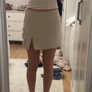 Beige linnekjol med slits - Snygg beige kortkjol i linne med enkel design och en liten slits framtill. Perfekt för varma dagar och lätt att matcha med olika toppar. Kjolen har en rak passform och känns både stilren och avslappnad.