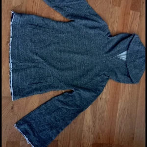 Grå hoodie från Exit Girls - Mysig grå hoodie från Exit Girls med lång ärm och stor huva. Tröjan har en enkel design med fickor framtill och är tillverkad i ett mjukt, stickat material. Perfekt för kyliga dagar när du vill vara både bekväm och stilren.