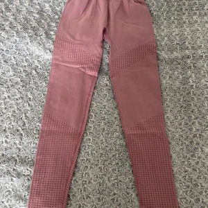 Rosa leggings med strukturdetaljer M - Säljer ett par rosa leggings i storlek M med snygga strukturdetaljer längs benen. De är stretchiga och har en hög midja, perfekta för träning eller chill. Materialet känns mjukt och följsamt mot huden.