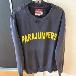 Mörkblå fleece-tröja Parajumpers - Mörkblå långärmad fleece-tröja från Parajumpers med stor gul logga framtill. Klassisk rund halsringning och ribbade muddar. Perfekt för dig som gillar streetwear och vill ha en skön och stilren tröja med tydlig branding.