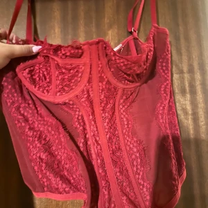Röd spetskorsett med meshdetaljer - Snygg röd korsett med spets och meshpaneler, justerbara axelband och hakknäppning bak. i storlek M men passar även folk som bär S 
