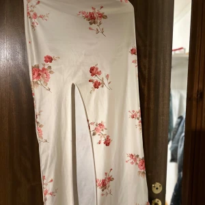 Vit långkjol med blommigt mönster - Vit långkjol med blommigt mönster och en slit vid benet. väldigt stretchigt material 