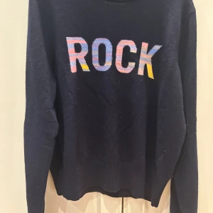 Mörkblå kashmirtröja ROCK Zadig & Voltaire - Snygg mörkblå stickad tröja från Zadig & Voltaire med färgglad 'ROCK'-text framtill. Tröjan är i mjuk kashmirblandning med lång ärm och rund hals. Perfekt för dig som gillar coola statement-plagg och vill ha något extra i garderoben.