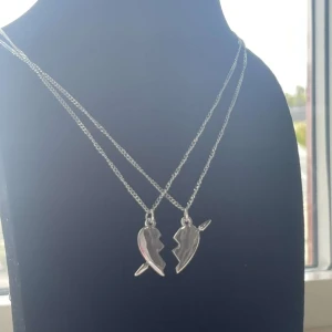 Krossat hjärta halsband silver - Två matchande halsband i silverfärg med varsin halva av ett brutet hjärta som hänge. Perfekt för dig och din bästis! Kedjorna är tunna och smidiga, och hjärthängena har en cool, kantig design.